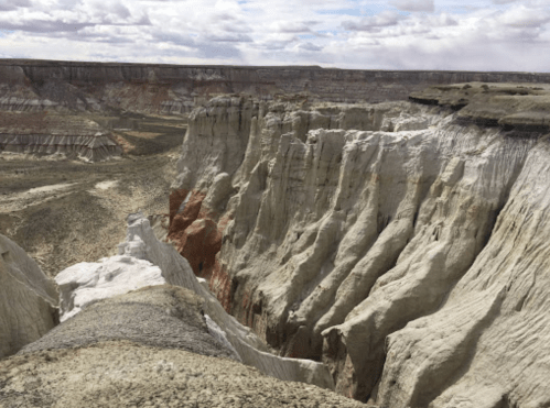 A dramatic landscape featuring layered cliffs and canyons under a cloudy sky, showcasing earthy tones and textures.