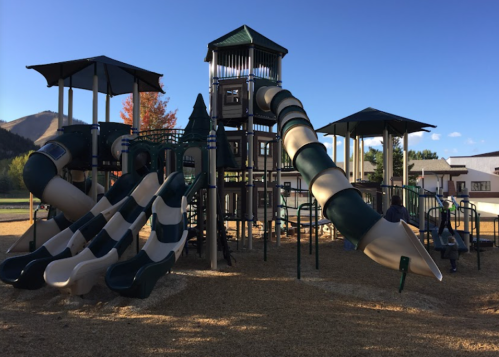 A colorful playground with multiple slides, climbing structures, and shaded areas, set against a clear blue sky.