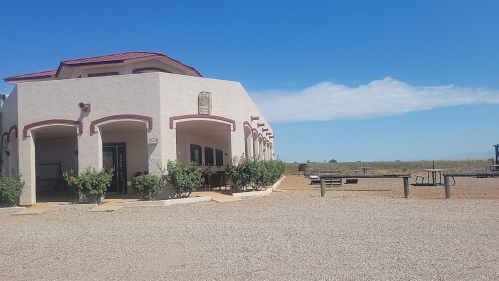 A modern building with a red roof and arched windows, surrounded by gravel and sparse vegetation under a clear blue sky.