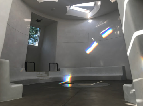 A modern, minimalist interior with curved white walls, natural light, and colorful light reflections on the floor.