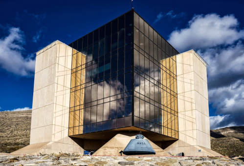 A modern, angular building with large glass windows, reflecting clouds and mountains, labeled "NASA" in the foreground.