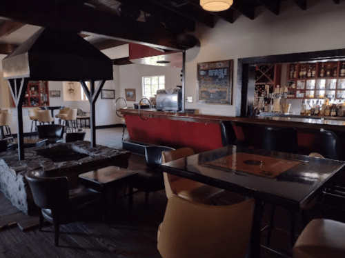 Cozy interior of a bar with a stone fireplace, tables, and a well-stocked bar in the background.