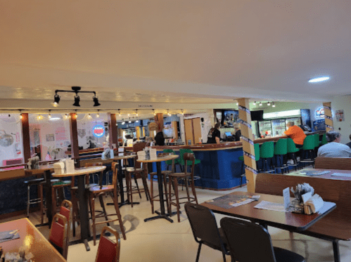 A casual restaurant interior with tables, a bar area, and patrons seated at the counter and tables.