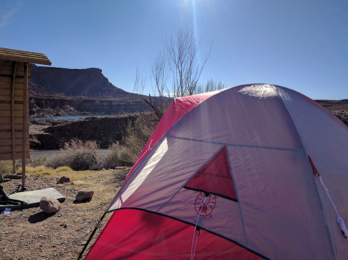 A red and gray tent set up outdoors, with a rocky landscape and clear blue sky in the background.