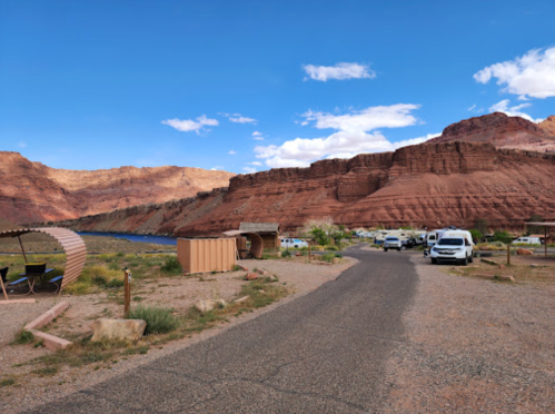 A scenic view of a campground with red rock formations, a winding road, and parked vehicles under a blue sky.