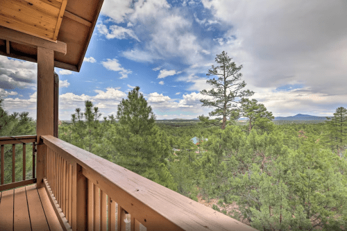 A wooden balcony overlooks a lush green landscape with trees and distant mountains under a partly cloudy sky.