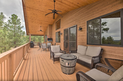 A wooden deck with comfortable seating, a table, and a view of trees, under a covered porch.