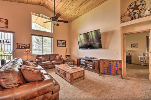 Cozy living room with a wooden ceiling, leather sofas, a coffee table, and a large TV on the wall.