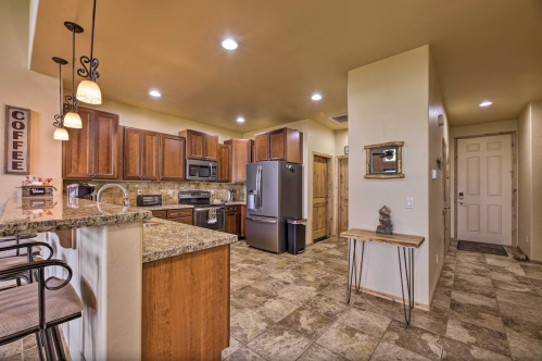 Modern kitchen with wooden cabinets, granite countertops, and stainless steel appliances, leading to a hallway and front door.