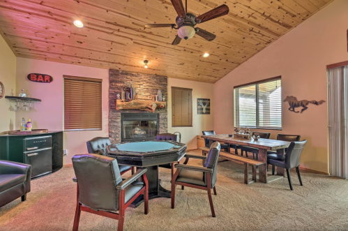 Cozy game room with a poker table, bar area, stone fireplace, and wooden dining table under a wooden ceiling.
