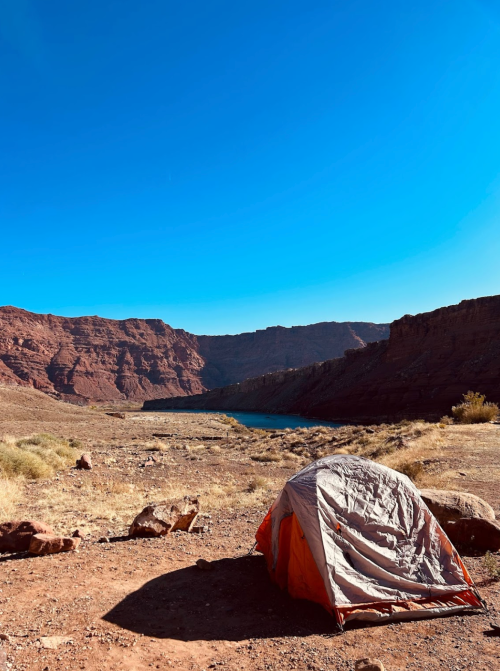 A tent set up in a desert landscape with rocky cliffs and a clear blue sky in the background.
