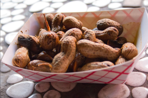 A paper tray filled with roasted peanuts on a textured surface.