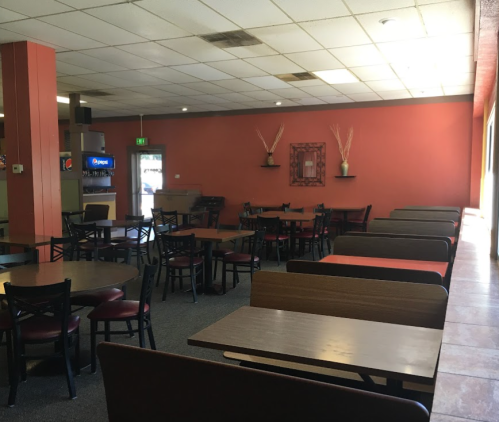 A spacious, empty dining area with tables and chairs, featuring warm orange walls and soft lighting.