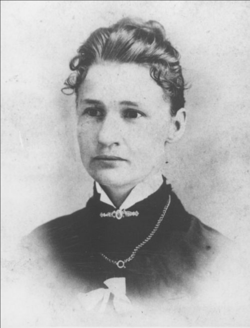 Black and white portrait of a woman with curly hair, wearing a dark dress and a necklace, looking directly at the camera.