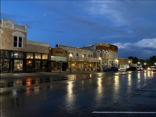 A quiet street scene at dusk, featuring historic buildings and reflections on a wet road.