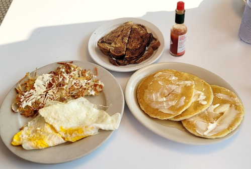 A plate with pancakes, an omelet, hash browns, and toast, accompanied by a bottle of hot sauce.