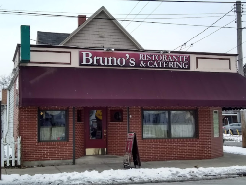 A brick restaurant with a maroon awning reading "Bruno's Ristorante & Catering," surrounded by snow.