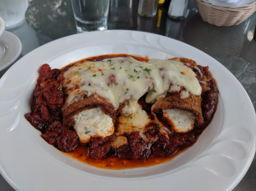 A plate of enchiladas topped with melted cheese, served in a rich red sauce with a sprinkle of herbs.