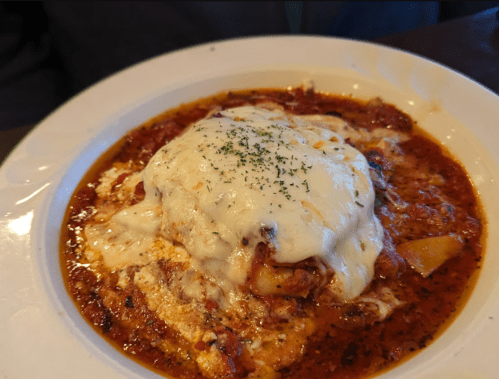 A plate of cheesy lasagna topped with herbs in a rich tomato sauce.