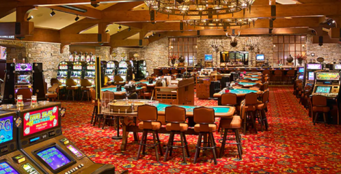 Interior of a casino featuring slot machines, card tables, and a rustic decor with stone walls and wooden beams.
