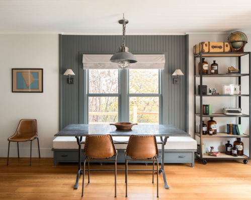 A modern dining area featuring a metal table, brown chairs, and a bookshelf with decor against a gray wall.