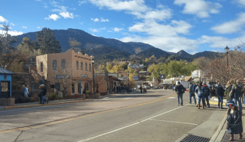 A scenic street in a small town with shops, people walking, and mountains in the background under a partly cloudy sky.