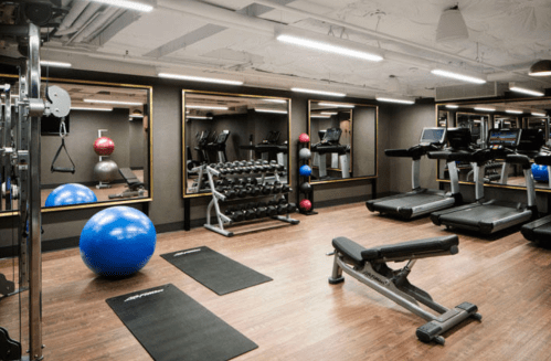 A modern gym with exercise equipment, including treadmills, weights, and a blue exercise ball, reflected in mirrors.