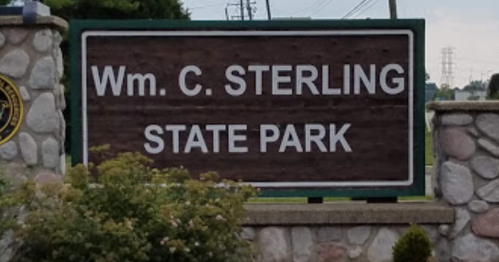 Sign for Wm. C. Sterling State Park, featuring a wooden design and stone base, surrounded by greenery.