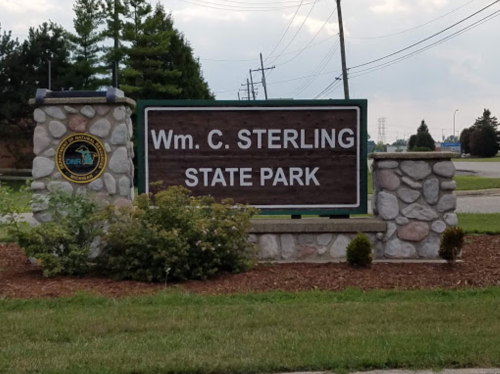 Sign for Wm. C. Sterling State Park, featuring stone pillars and greenery, with power lines in the background.