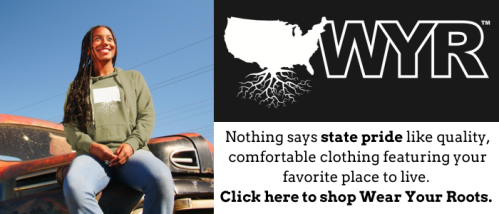 A smiling woman in a hoodie sits on a vintage truck, promoting state pride clothing with the text "Wear Your Roots."