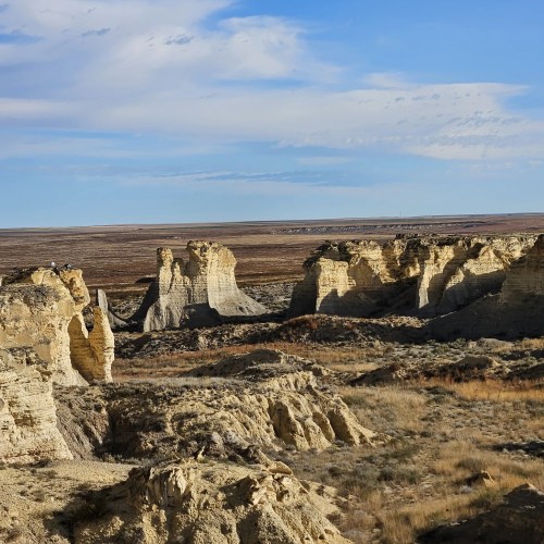 A vast landscape featuring unique rock formations under a blue sky with scattered clouds.