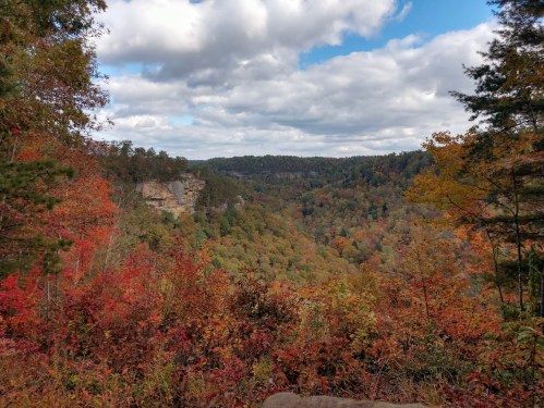 A scenic view of a colorful autumn landscape with cliffs and rolling hills under a partly cloudy sky.