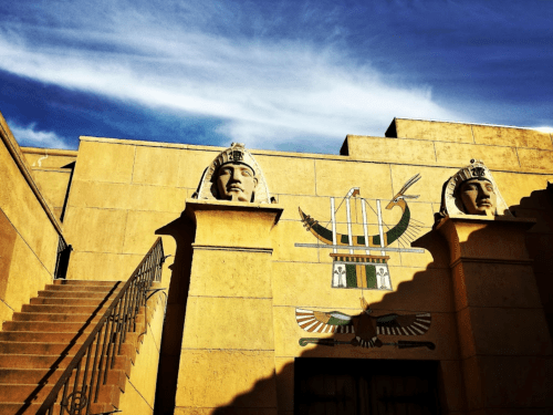 Ancient Egyptian-style building with two large stone heads and decorative hieroglyphs under a blue sky.