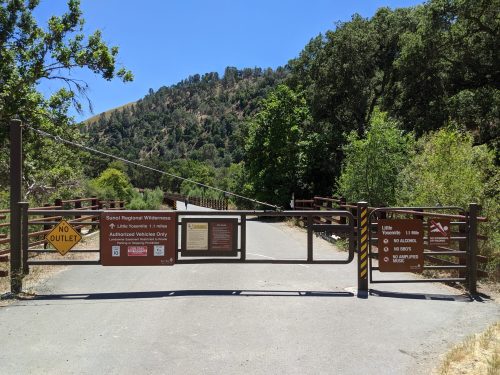 A closed gate at the entrance to a wooded area, with signs indicating no outlet and authorized vehicles only.