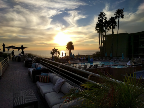 Sunset over a poolside area with palm trees, lounge seating, and umbrellas, creating a serene coastal atmosphere.