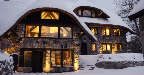 A cozy stone house with a thatched roof, illuminated at night, surrounded by snow-covered landscape.