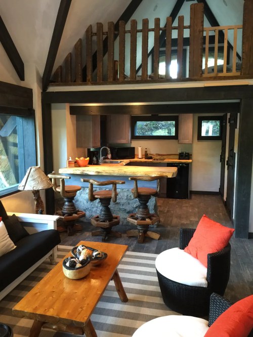 Cozy interior of a cabin with a loft, featuring a kitchen, seating area, and rustic decor.