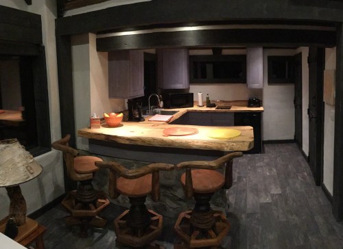 A modern kitchen with a wooden island, bar stools, and purple cabinets, featuring a cozy, rustic design.