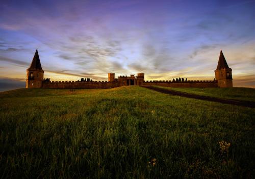 A majestic castle with two tall towers, set against a colorful sunset sky, surrounded by lush green grass.