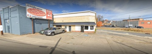 A street view of a building with a Little Caesars sign and a parked vehicle in front, surrounded by a parking lot.