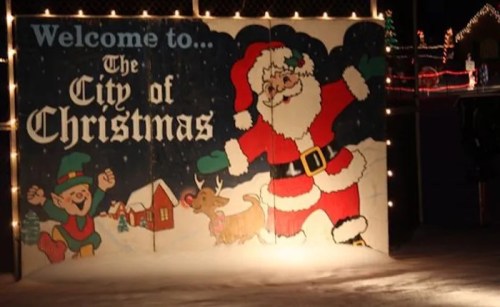 A festive sign reading "Welcome to the City of Christmas," featuring Santa, an elf, and a reindeer.