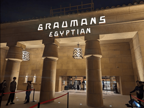 Exterior of Grauman's Egyptian Theatre at night, featuring illuminated signage and a queue of people outside.