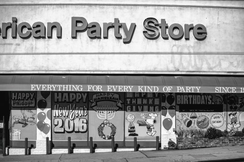 Black and white image of a party store facade with festive decorations and signs for various holidays and events.