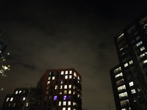 Two buildings at night, with illuminated windows against a dark, cloudy sky.