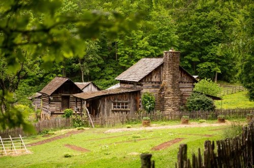 A rustic wooden farmhouse surrounded by lush greenery and a wooden fence, set in a tranquil rural landscape.