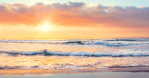 A serene beach at sunset, with gentle waves and a colorful sky illuminated by the sun's rays.