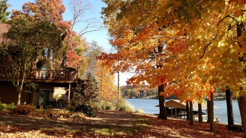 A scenic view of a lakeside home surrounded by vibrant autumn foliage and a calm waterway.