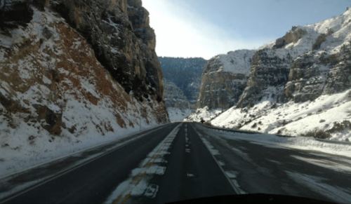 A snow-covered highway flanked by steep, rocky cliffs under a clear blue sky.