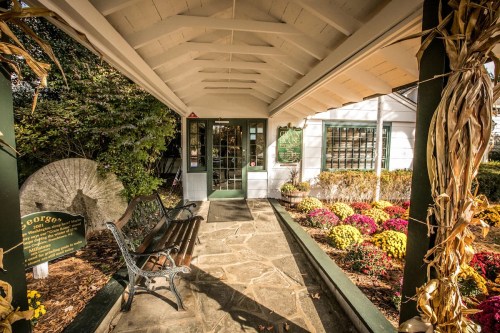 A charming entrance with a stone path, bench, and colorful flowers leading to a white building under a covered porch.