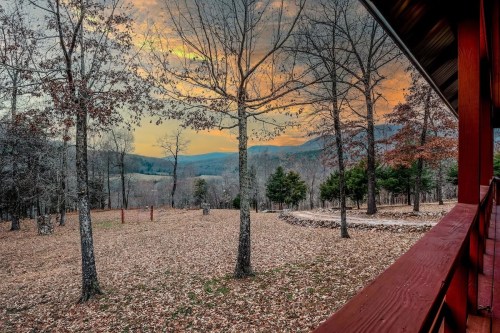 A serene landscape with trees and a stone circle, set against a colorful sunset over rolling hills.